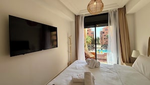 A hotel room with a large bed, a flat-screen TV mounted on the wall, a balcony with curtains, and a hanging light fixture. - Menara Palms Marrakech (Marrakech)