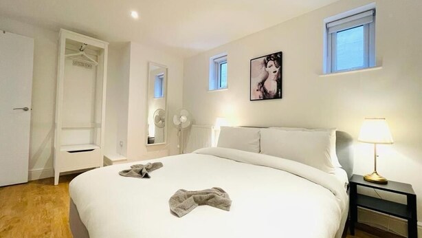 A bedroom with a large bed, a bedside table with a lamp, a wardrobe, and a window. - Prosper House Apartment 1 - Stylish City living (Norwich)