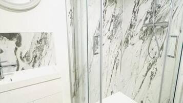 Une salle de bain moderne avec une douche à parois de verre, des murs en marbre blanc et un plancher en bois.