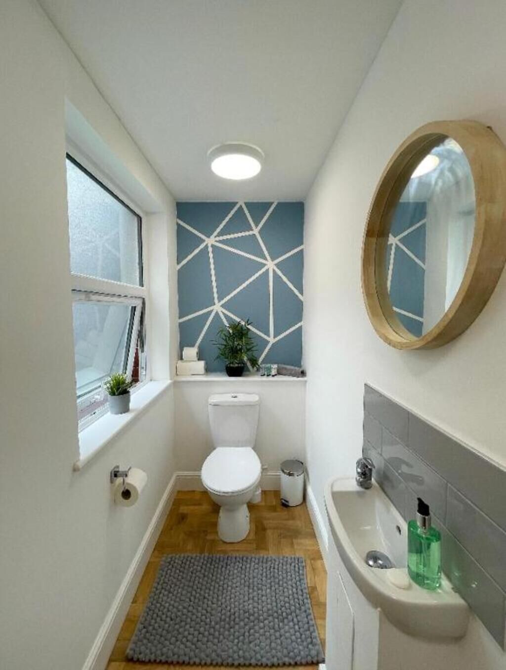 Un bagno compatto con un water bianco, un lavabo con specchio, una finestra con vista e un motivo geometrico sulla parete.