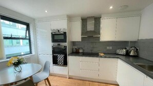 A modern kitchen with white cabinets, a black countertop, and a window providing a view of the outside. - Prosper House Apartment 1 - Stylish City living (Norwich)