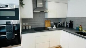 A modern kitchen with white cabinets, a black oven, and a grey tiled backsplash. - Prosper House Apartment 1 - Stylish City living (Norwich)