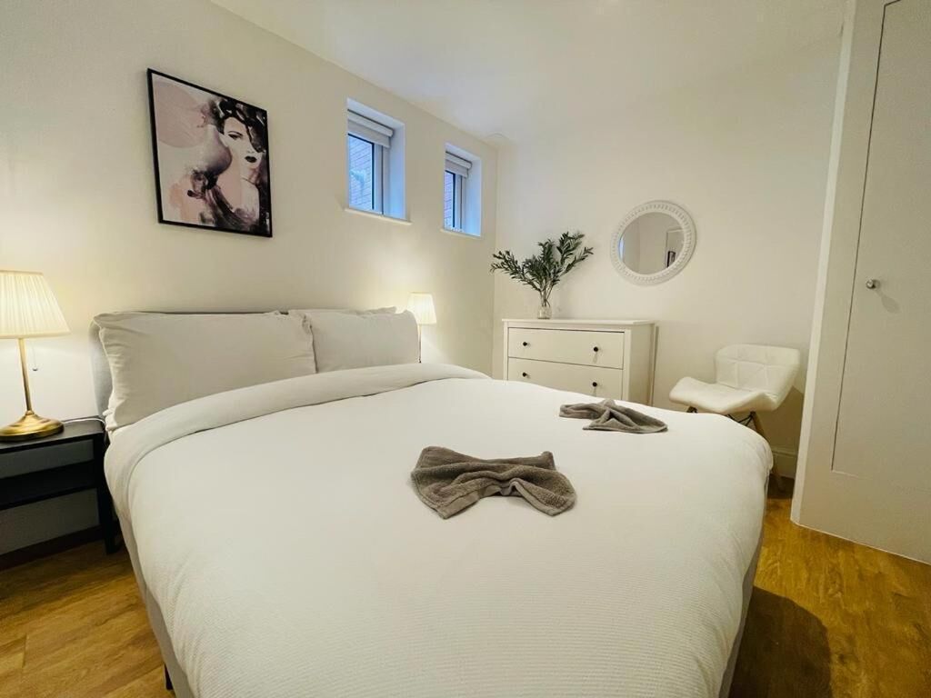 A bedroom with a large bed, a bedside table with a lamp, a dresser, a chair, and a painting on the wall.