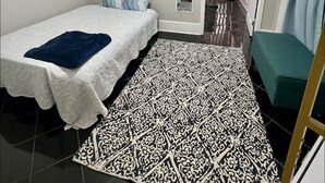 A small, neatly arranged bedroom with a single bed, a bedside table, a mirror, and a patterned rug. - Mardi Gras special garden district (New Orleans)