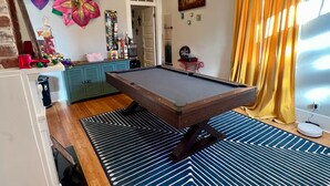 A pool table in a room with wooden flooring, a patterned rug, and a ceiling light. - Mardi Gras special garden district (New Orleans)