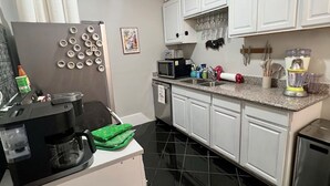 A kitchen with white cabinets, a black refrigerator, a coffee maker, and a microwave. - Mardi Gras special garden district (New Orleans)