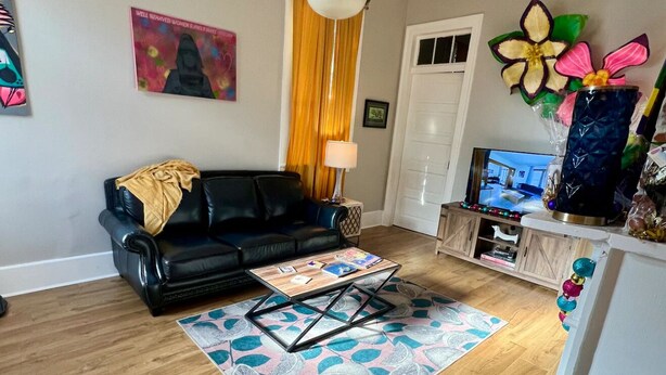 A living room with a black leather sofa, a wooden coffee table, a patterned rug, and a television on a wooden cabinet. - Mardi Gras special garden district (New Orleans)