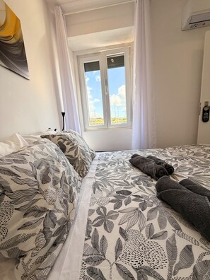 A bedroom with a bed, a window with curtains, and a wall-mounted phone. - Naval Marina View Apartment 1 (Vila do Conde)