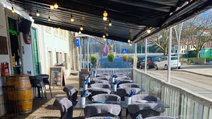 Un café al aire libre con mesas y sillas, algunas con manteles y otras con individuales.