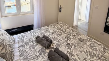 A bedroom with a bed, a window with curtains, an air conditioning unit, and a view of boats and water outside.