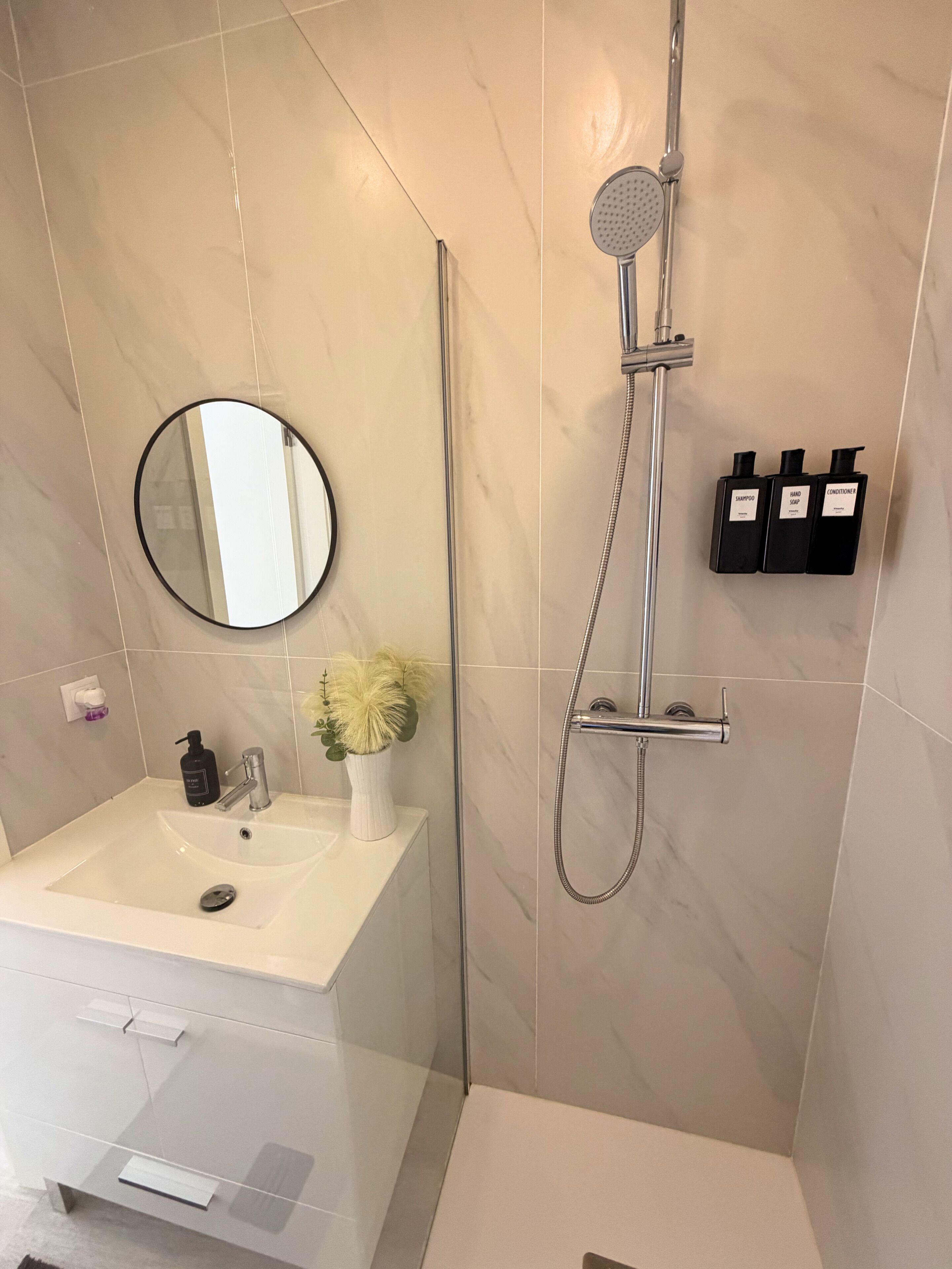Ein modernes Badezimmer mit Waschbecken, Spiegel, Duschbrause und Pflegeprodukten.