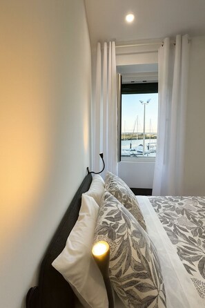 Une chambre d’hôtel avec un lit, une fenêtre avec des rideaux et une vue sur des bateaux et un port de plaisance.