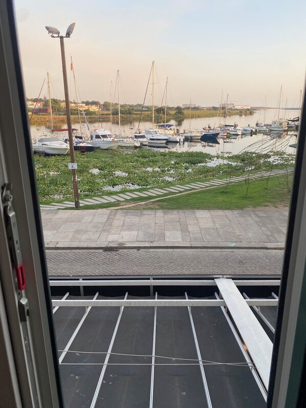 Vista desde el interior de un edificio hacia un puerto deportivo con barcos amarrados, un área verde y un camino pavimentado.