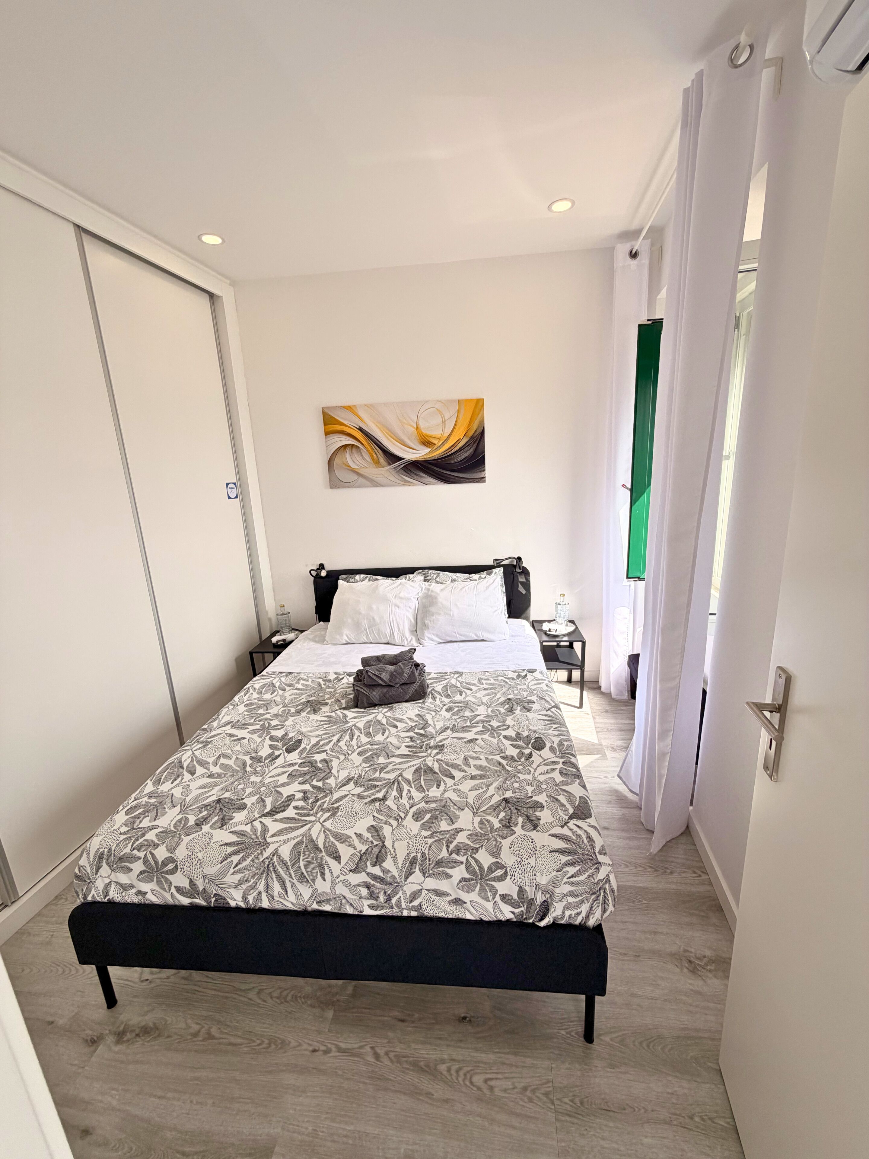 A bedroom with a bed, a nightstand, a wall art piece, and a door.