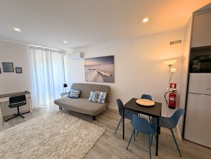 Una sala moderna con sofá, mesa de comedor con sillas, televisor de pantalla plana y refrigerador.
