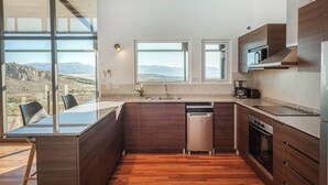 A modern kitchen with a large island, built-in appliances, and a view of mountains. - Casa Altos del Ñirihuau - Panoramic Refuge (Dina Huapi)