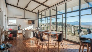 A spacious room with a large dining table, chairs, and a view of the countryside through large windows. - Casa Altos del Ñirihuau - Panoramic Refuge (Dina Huapi)