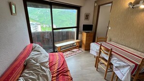 Un dormitorio con cama, escritorio y silla. Se ve follaje verde a través de la ventana.