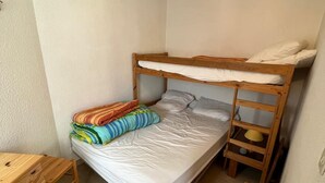 Una habitación pequeña con una cama individual de madera, un escritorio de madera y un pequeño taburete de madera.