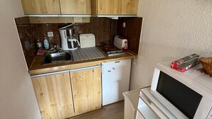 Una cocina compacta con armarios de madera, un lavamanos, una cafetera, un tostador, un microondas y un refrigerador pequeño.