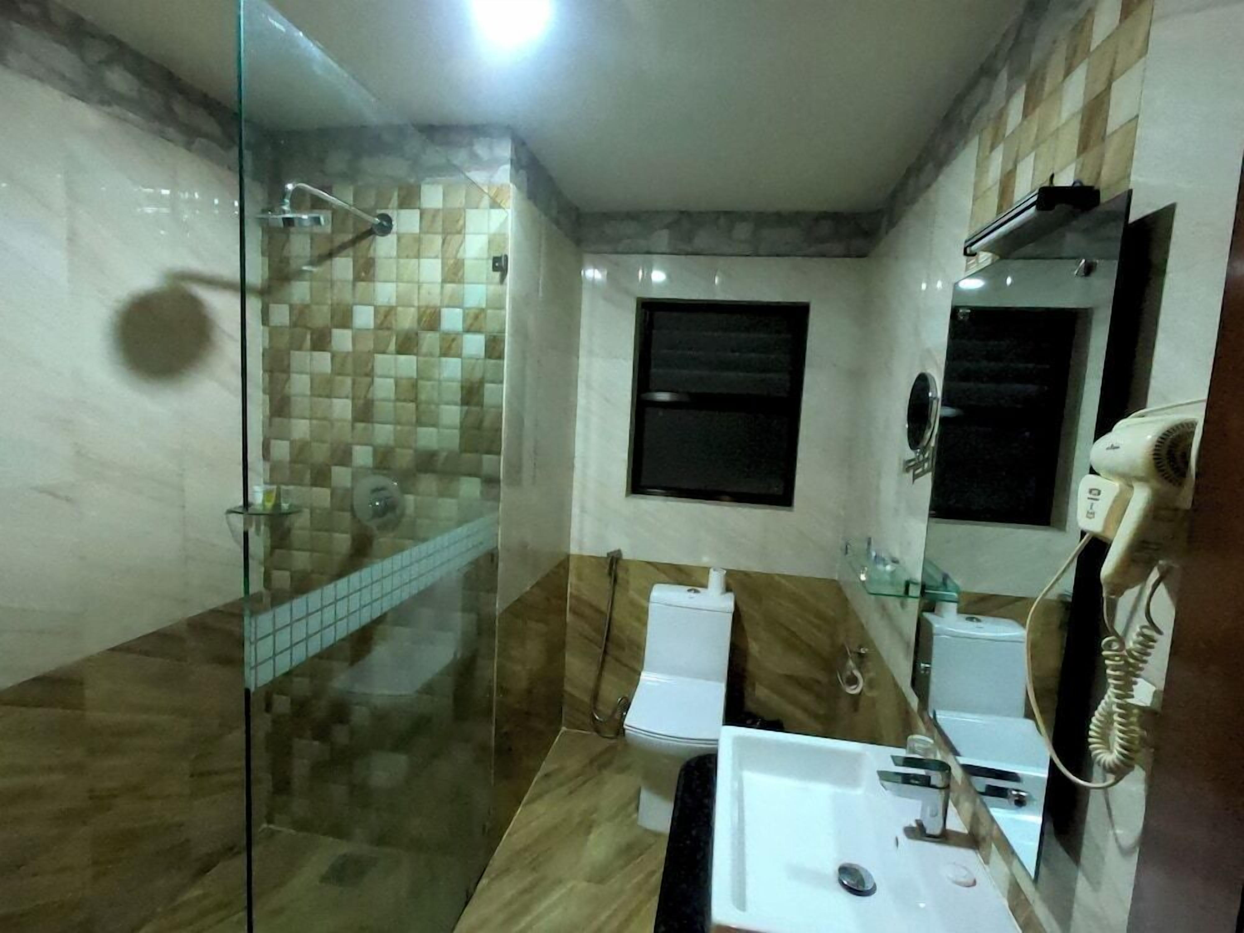 Ein Badezimmer mit Duschkabine aus Glas, Toilette, Waschbecken und Fön.