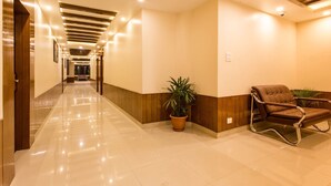 A hotel lobby with a long corridor, wooden paneling, a seating area with a brown leather chair, and a potted plant. - Hotel Buddy (Kathmandu)