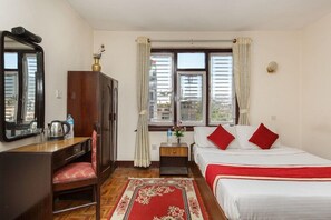 Une chambre d’hôtel comprenant un lit, un bureau avec une chaise, une armoire, une fenêtre avec des rideaux et un tapis rouge.