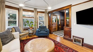 A living room with a sofa, armchair, ottoman, and a large window with curtains. - Gorgeous private home! Central Air 4 beds, hot tub, patio, designer furnishings (Portland)