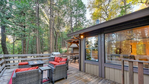 Una terraza con mobiliario de mimbre y una parrilla de barbacoa, rodeada de un bosque.