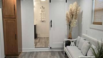 A room with a sliding door leading to a bathroom, a white sofa, a wooden cabinet, and a potted plant.