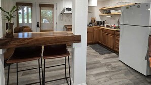 A modern kitchen with a wooden dining table and bar stools, a white refrigerator, and wooden cabinets.
