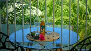 Une table en verre avec une bouteille et des verres, placée devant un décor de palmiers et offrant une vue sur l’océan.