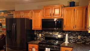 Une cuisine avec des meubles de rangement en bois, un réfrigérateur noir, un four à micro-ondes et une cuisinière.