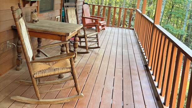 Une terrasse en bois avec des fauteuils à bascule et une table, donnant sur une forêt.