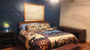 Une chambre à coucher comprenant un lit, une table de chevet, un banc, un ventilateur de plafond et un luminaire fixé au mur.