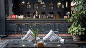 A bar area with a bartender, stools, a counter with various bottles, and a sign for 'illy'. - Nepali Ghar Hotels & Resort (Kathmandu)