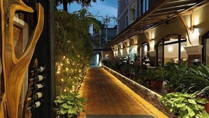 A corridor with a wooden sculpture, potted plants, and string lights leading to a building entrance. - Nepali Ghar Hotels & Resort (Kathmandu)