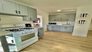 A kitchen with light grey cabinets, a stainless steel stove, and a wooden floor.