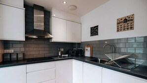 Una cocina moderna con armarios blancos, encimera negra, campana extractora de acero inoxidable, máquina de café y cartel con la carta de café en la pared.