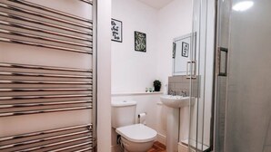 Un baño con inodoro, lavamanos y ducha. Hay cuadros en la pared.
