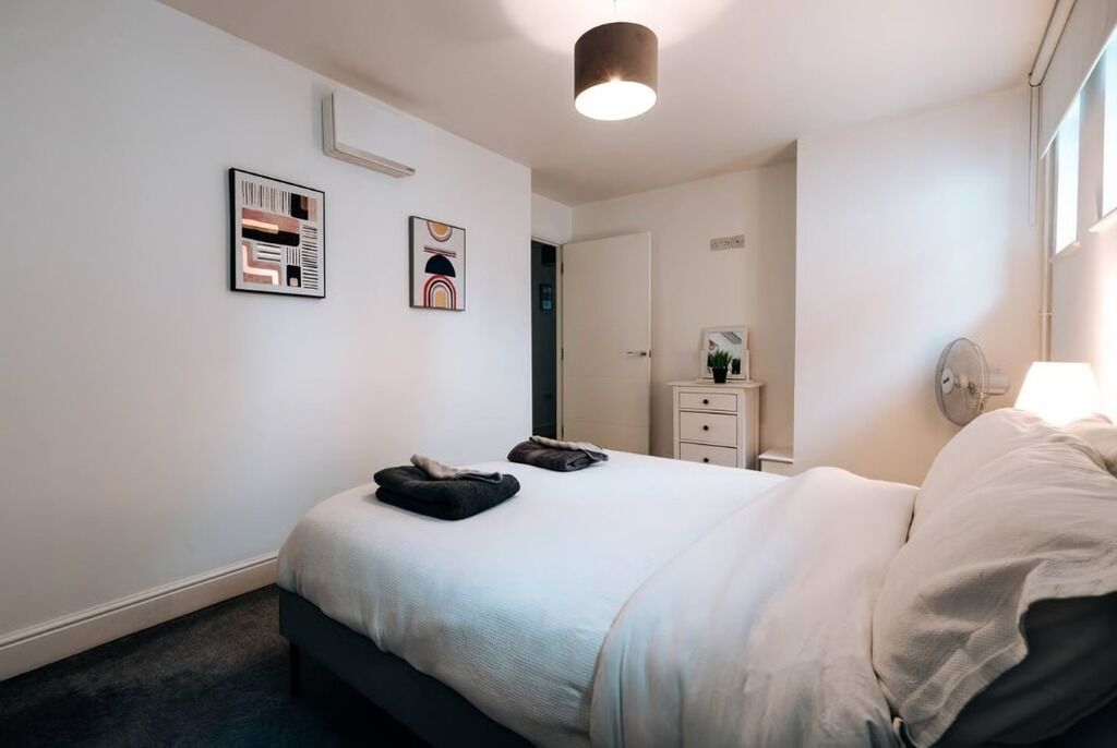 A bedroom with a bed, a bedside table, a mirror, and two framed artworks on the wall.