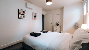 A bedroom with a bed, a bedside table, a mirror, and two framed artworks on the wall.