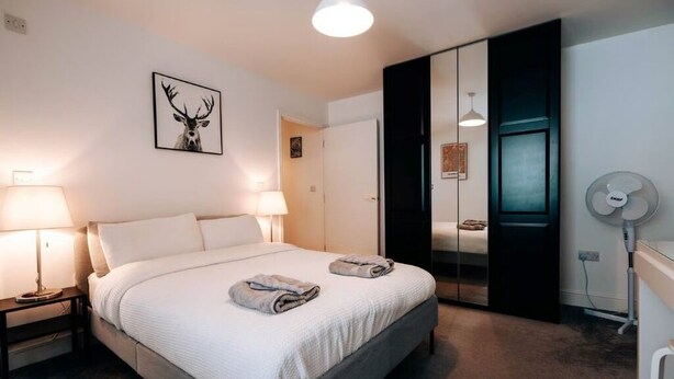 Un dormitorio moderno con una cama grande, dos lámparas de noche, un espejo, una luz de techo y un ventilador de pared.