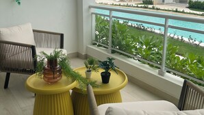 A balcony with wicker furniture, a yellow table with potted plants, and a view of a swimming pool and buildings in the background. - Beauty Apartment Dominicus Breeze (Dominicus)