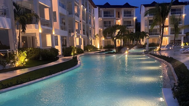 A swimming pool with a curved edge, surrounded by multi-story buildings with balconies and outdoor seating areas. - Beauty Apartment Dominicus Breeze (Dominicus)