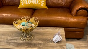 A brown leather sofa with a yellow pillow that has the word "home" on it. In front of the sofa, there is a wooden coffee table with a decorative basket and a small white object on it. - Charming 2-bedroom townhome in delightful Murrieta with AC (Murrieta)
