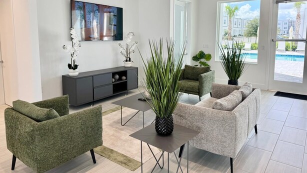 Een moderne woonkamer met een grijze bank, een groene fauteuil, een salontafel en een groot raam met uitzicht op een zwembad.