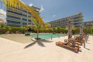 A poolside area with lounge chairs and umbrellas, surrounded by palm trees and a large building with multiple balconies. - Oceanfront, serenity and security with wifi and private beach (Cartagena)