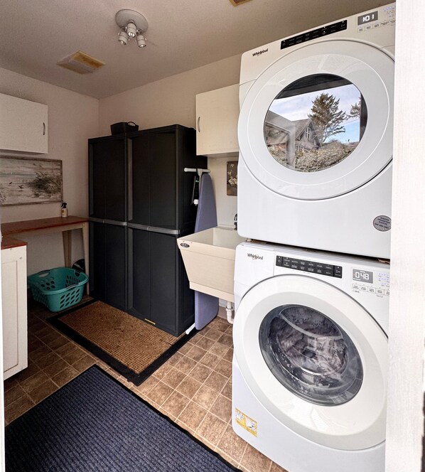 A compact laundry area with stacked washers and dryers, a refrigerator, and a small sink. - Ocean Cove Inn #7 - Ocean View (Yachats)