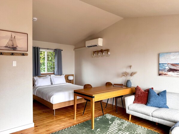 Une chambre à coucher avec un lit en bois, une table en bois, un canapé gris et un tableau représentant un bateau accroché au mur.